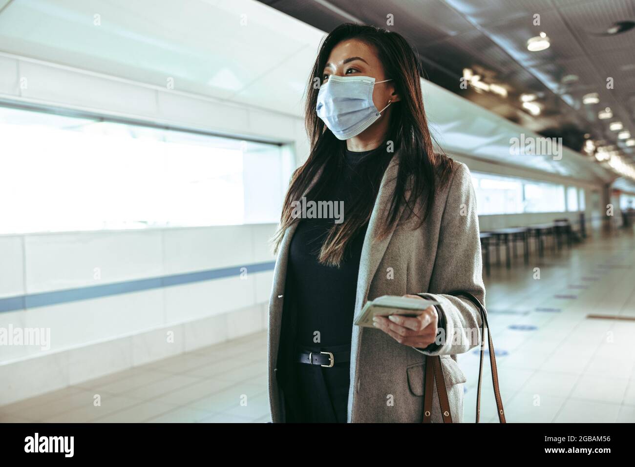 Uomo d'affari che indossa maschera protettiva per il viso in viaggio in aria. Una donna che cammina attraverso il corridoio vuoto dell'aeroporto durante la pandemia. Foto Stock