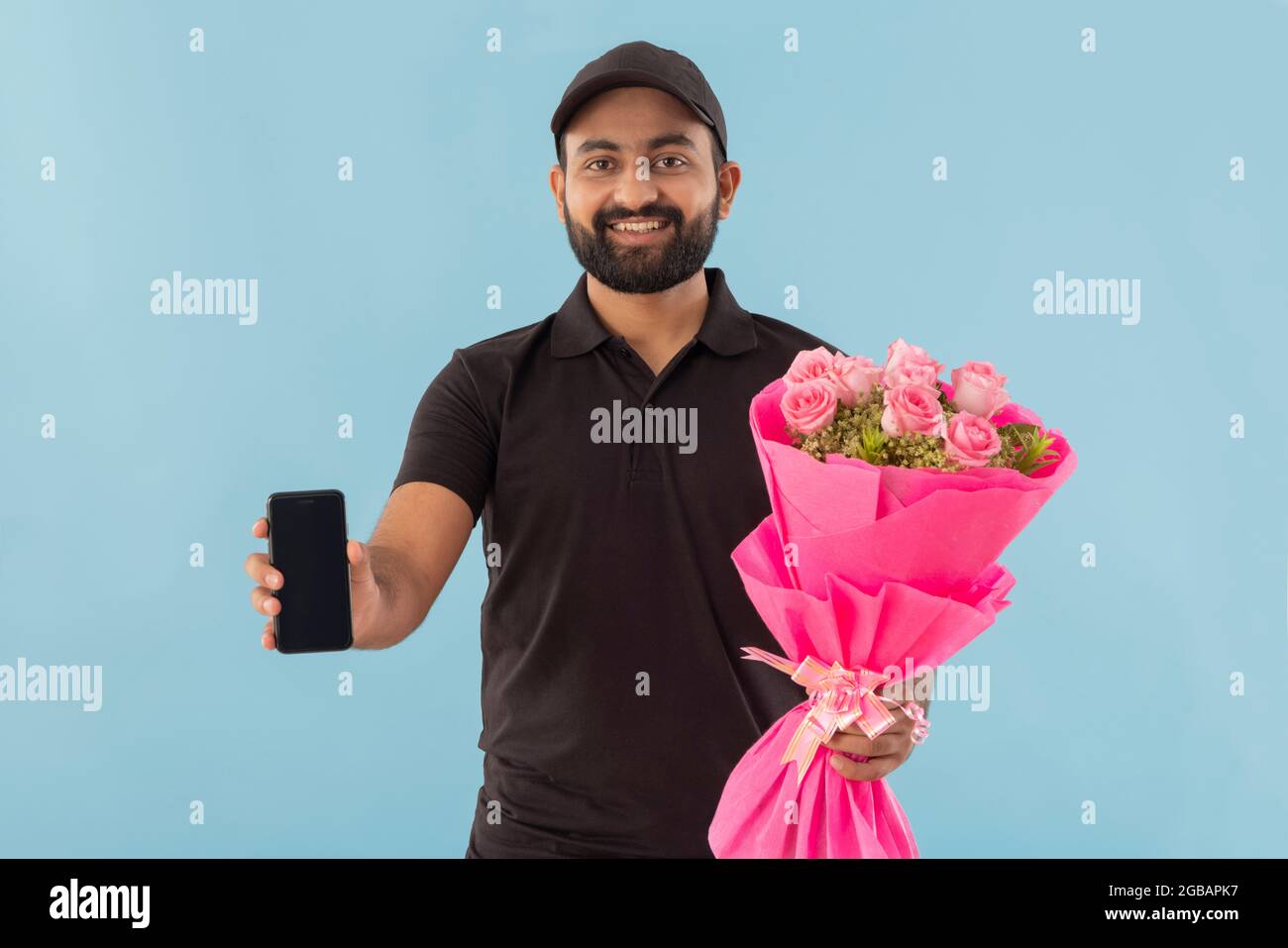 UN RAGAZZO DI CONSEGNA DEL FIORE CHE TIENE FELICEMENTE IL BOUQUET E IL TELEFONO MOBILE Foto Stock