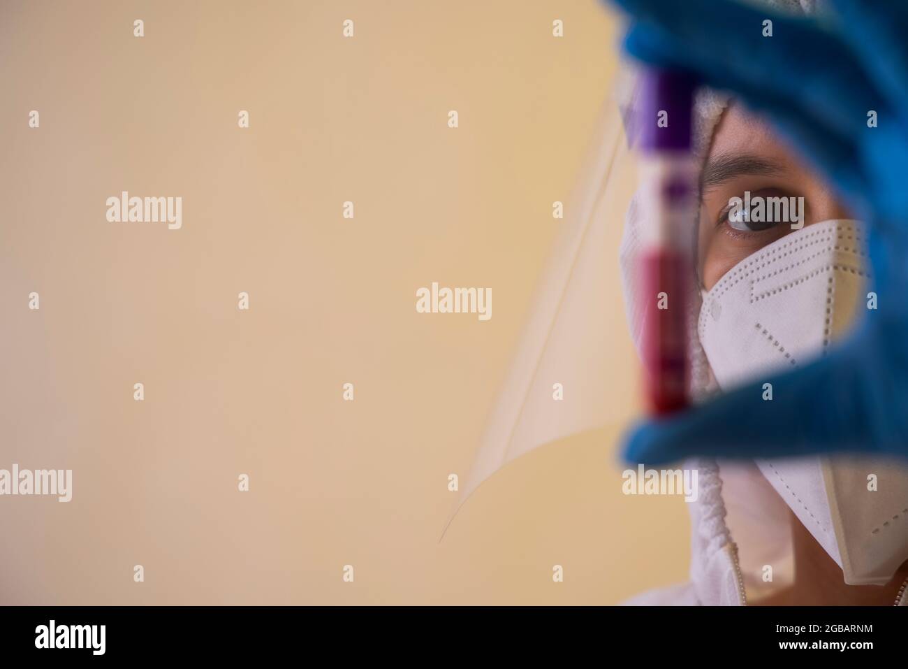 Un medico con schermo facciale che contiene un flacone di campione di sangue. Foto Stock