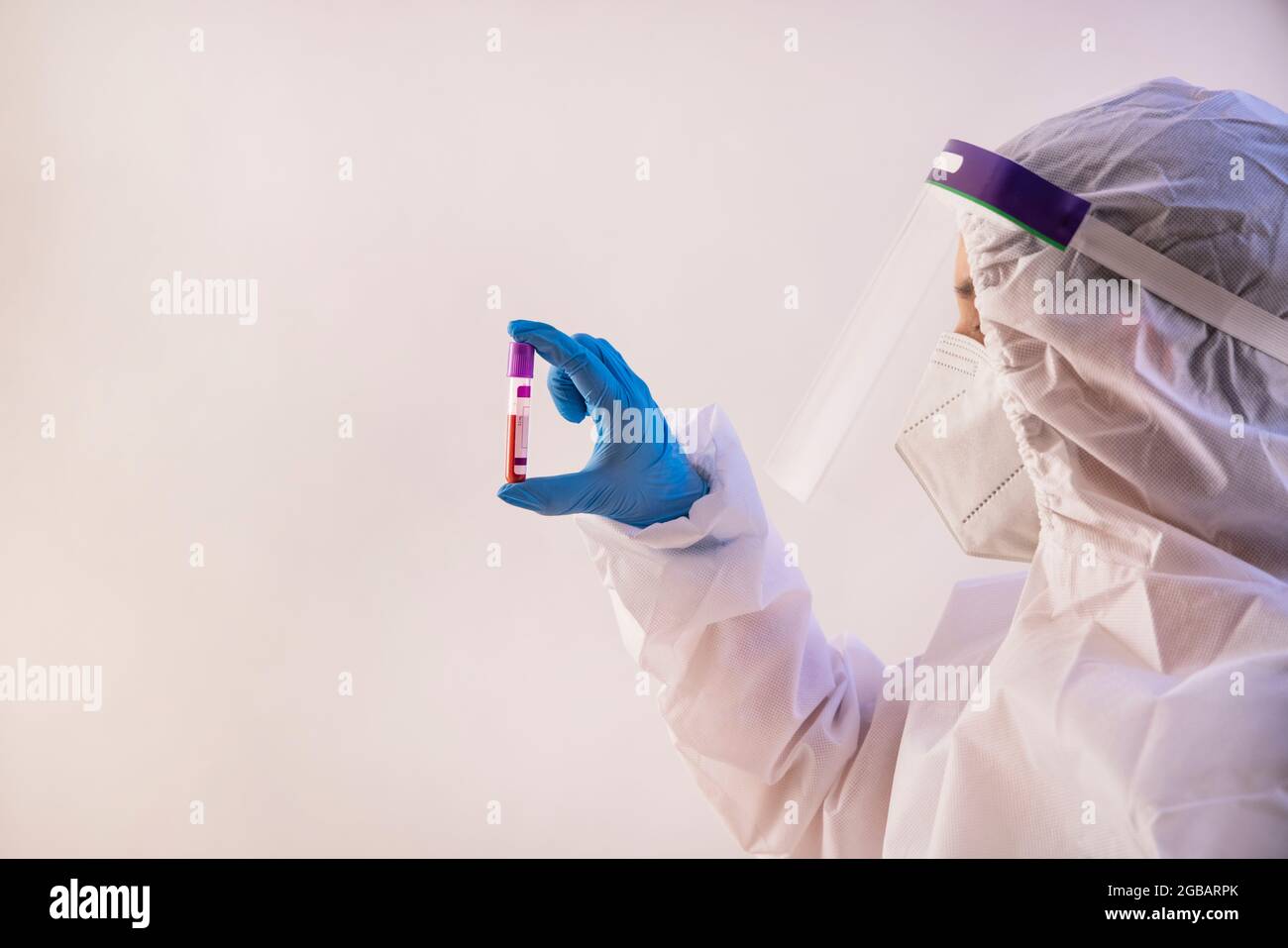 Un medico che indossa un kit PPE contenente un flacone di campione di sangue. Foto Stock