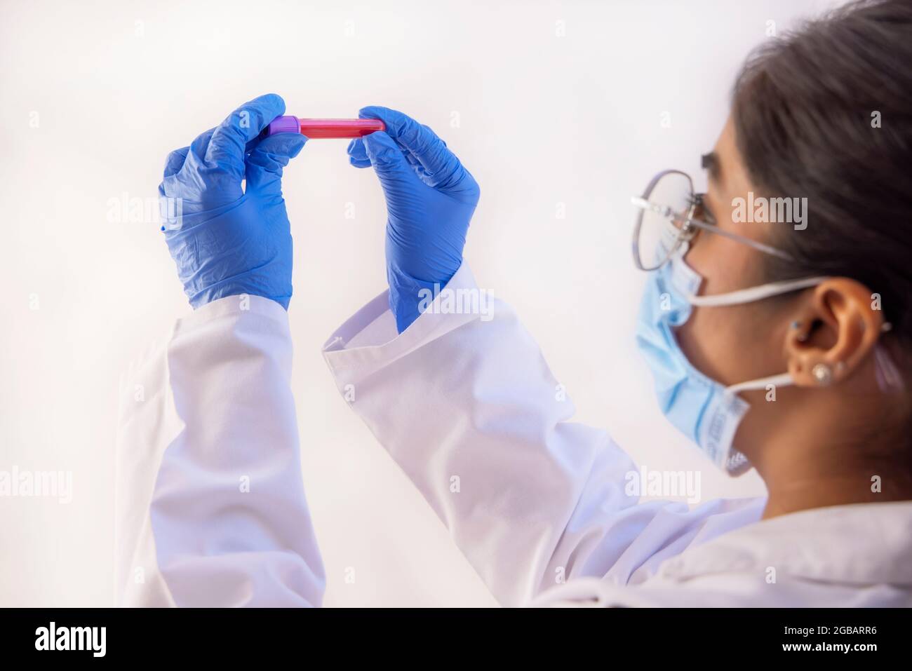 Un medico che indossa una maschera facciale che contiene un flacone di campione di sangue. Foto Stock
