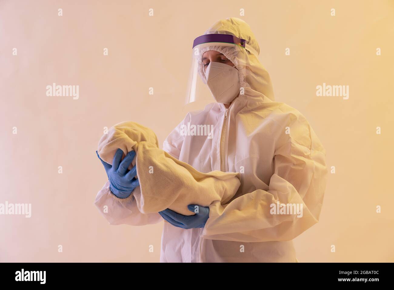 Un operatore sanitario in kit PPE che tiene un bambino in armi. Foto Stock