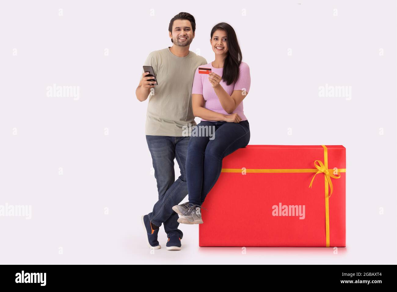 Una giovane donna seduta su uno sgabello a forma di regalo con un uomo accanto, mostrando carta di credito e telefono. Foto Stock