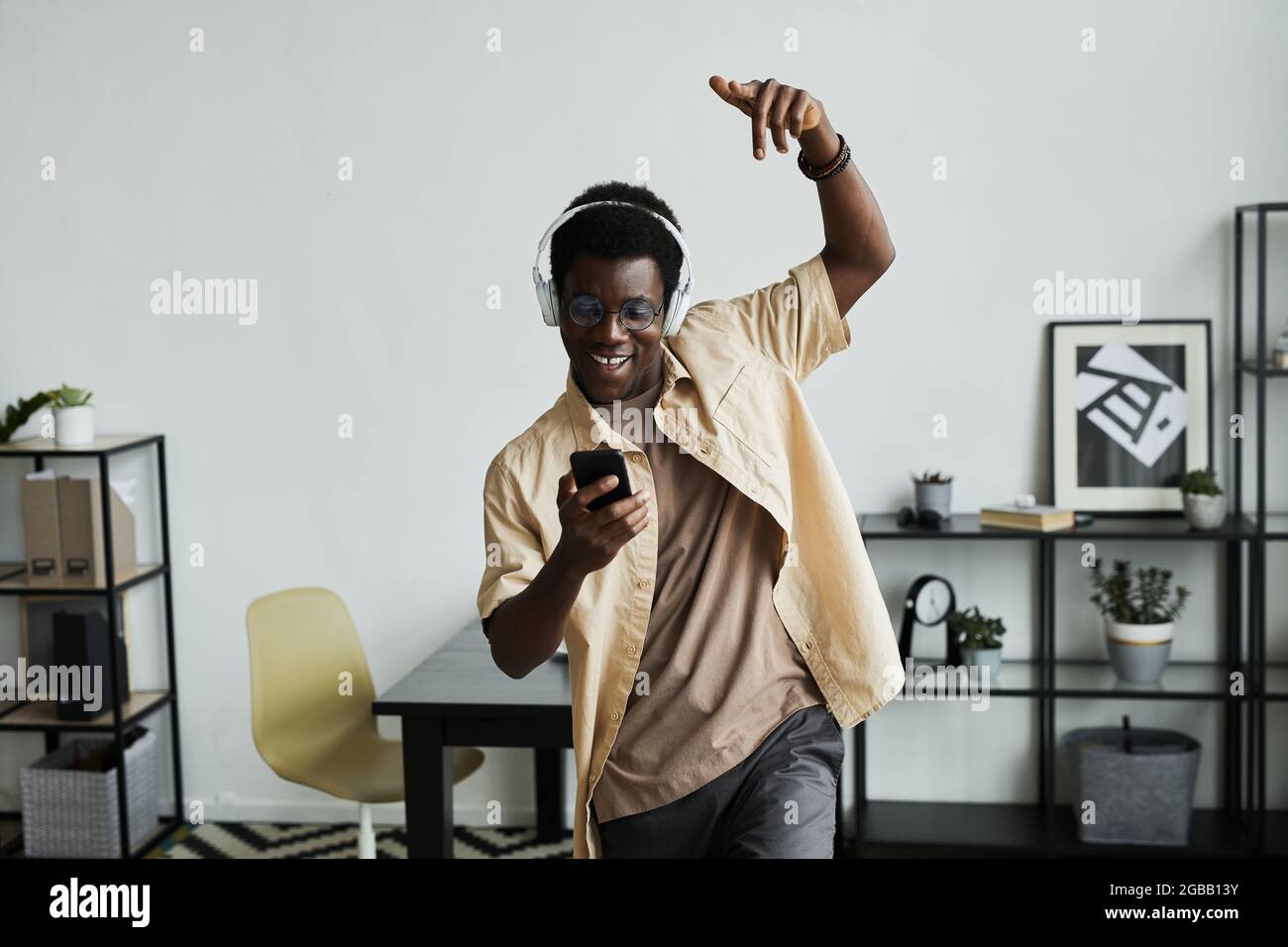 Uomo africano felice in cuffia utilizzando il suo telefono cellulare per ascoltare musica e ballare a casa Foto Stock