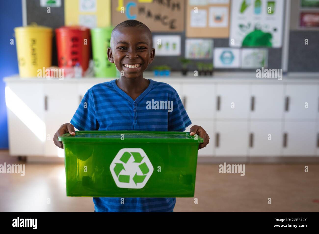 Ritratto del ragazzo afroamericano che tiene vassoio riempito con articoli di plastica riciclabili a scuola Foto Stock