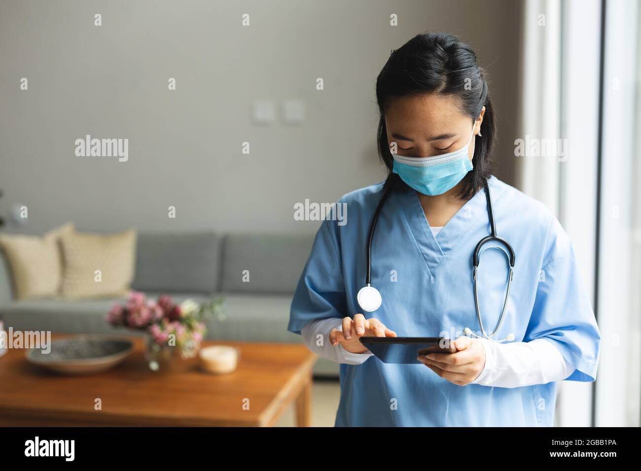 Fisioterapista femminile asiatica che indossa la maschera facciale e usa la compressa a casa prima del trattamento Foto Stock