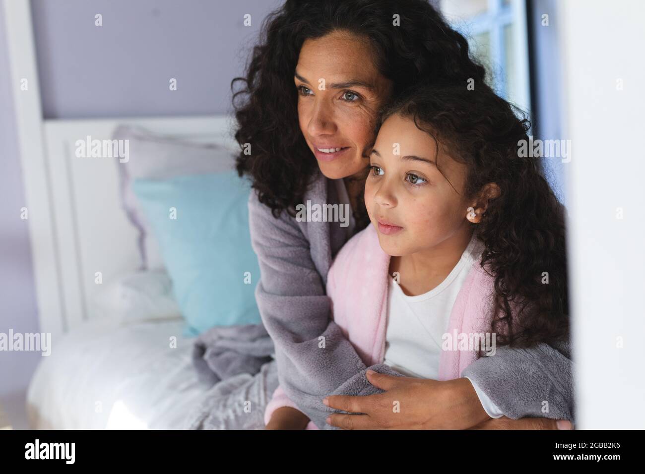 Felice razza mista madre e figlia seduta sul letto e abbracciando Foto Stock