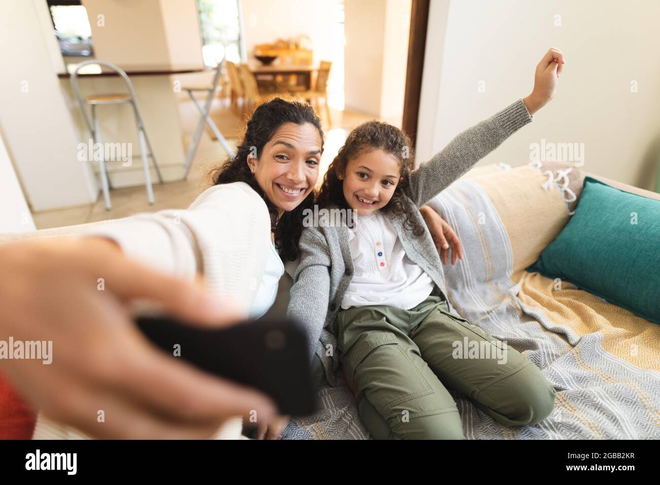 Misto razza madre e figlia seduta sul divano facendo facce divertenti, prendendo selfie Foto Stock