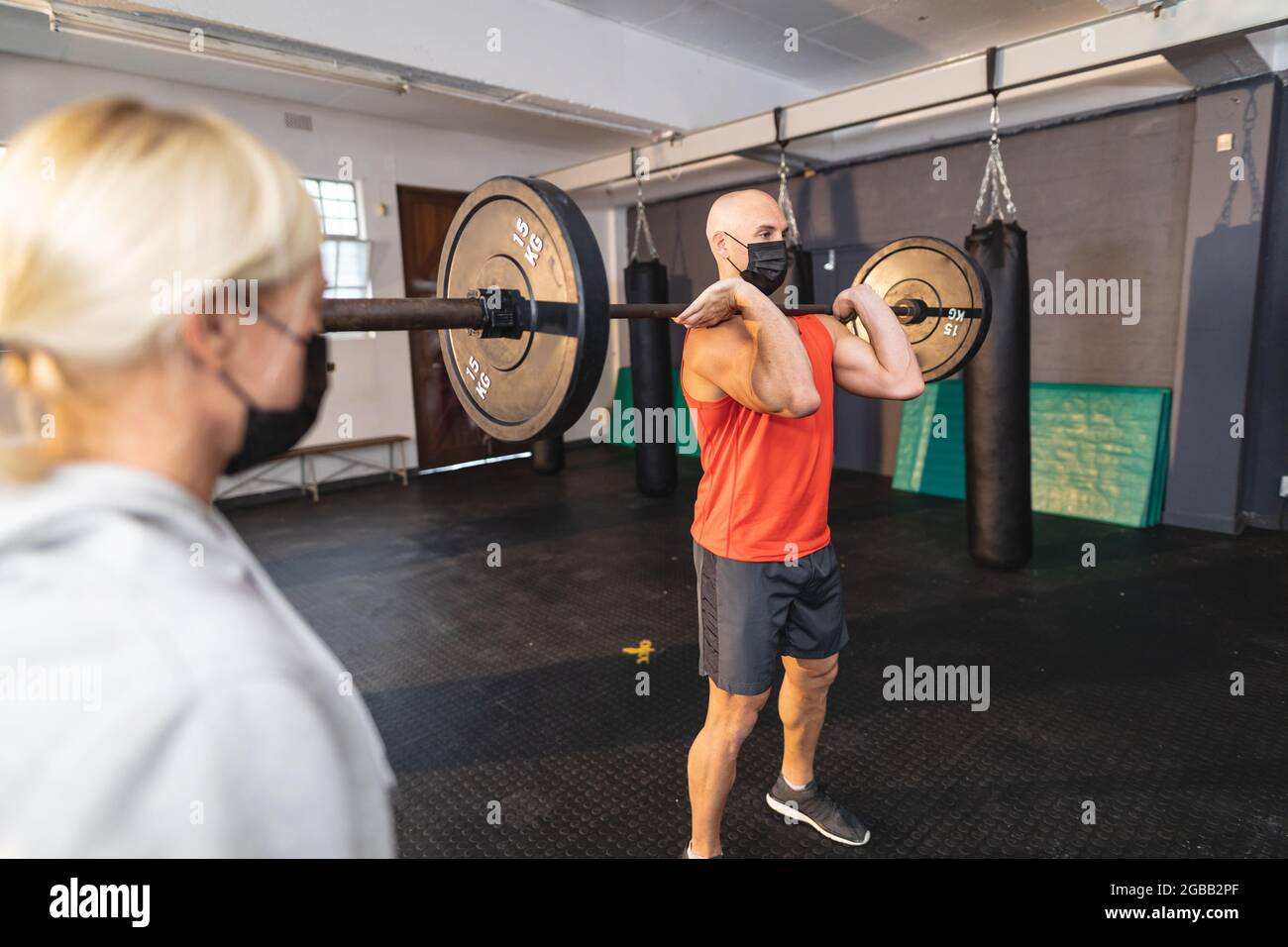 L'addestratore femmina caucasico istruisce l'uomo che si esercita alla palestra che indossa le maschere del viso, i pesi di sollevamento Foto Stock