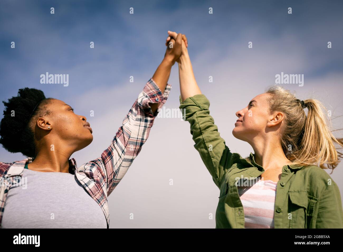 Due amici femminili felici e diversi che tengono le mani nella giornata di sole Foto Stock