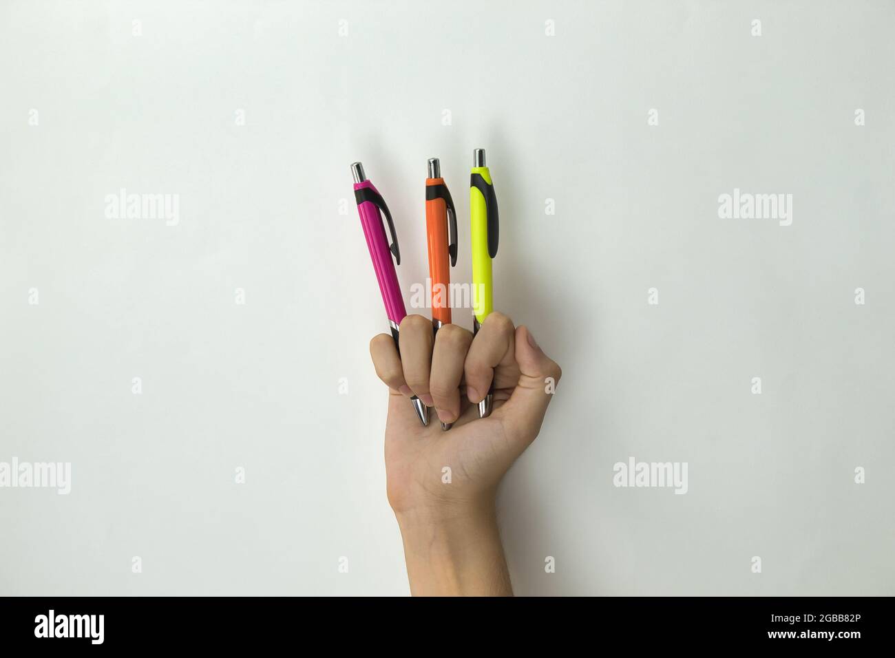 mano di una ragazza che tiene tre penne di un colore diverso tra le dita su sfondo bianco Foto Stock