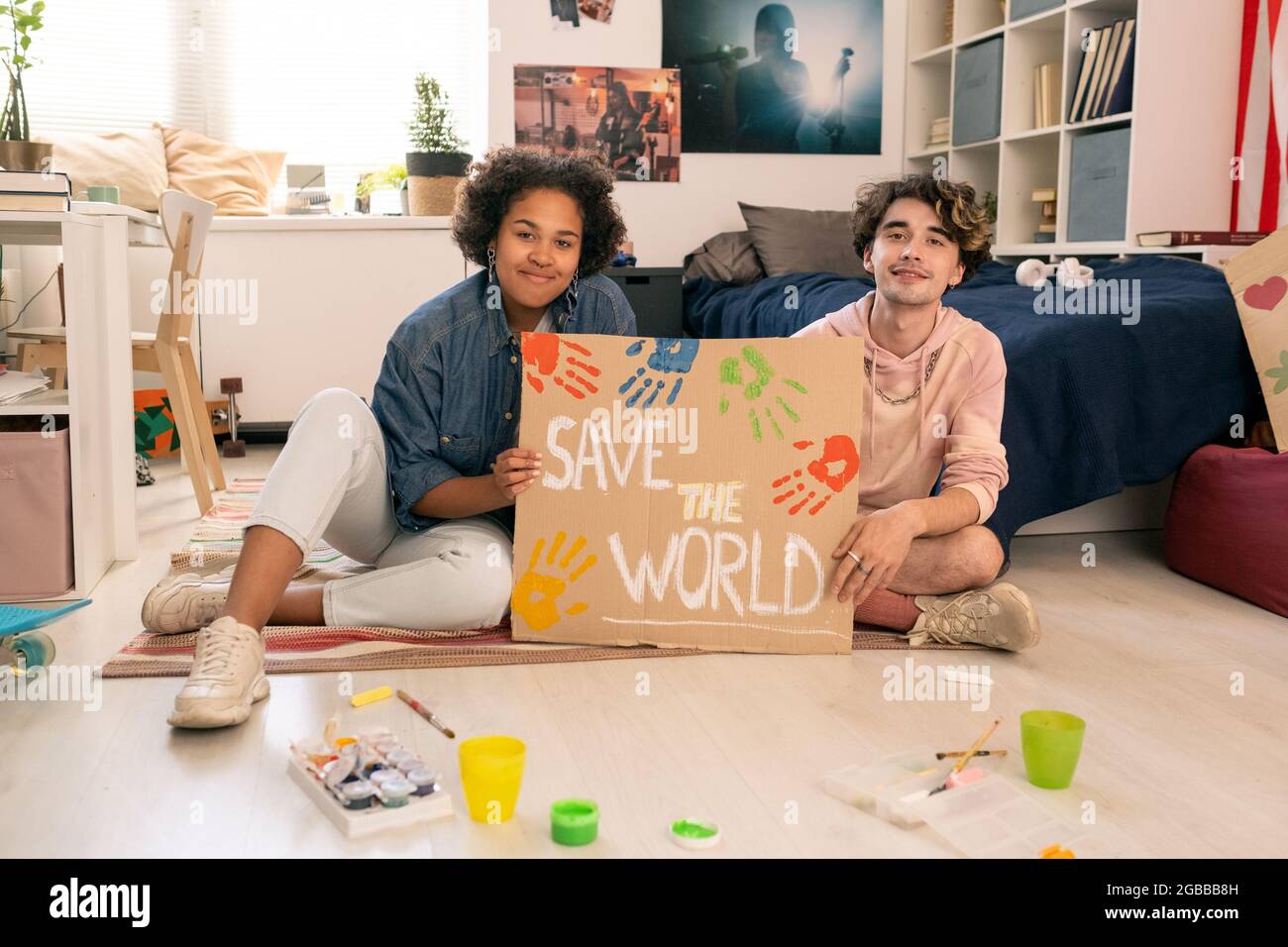 Adolescenti felici che mostrano un cartello fatto a mano mentre si siede sul pavimento in camera da letto Foto Stock