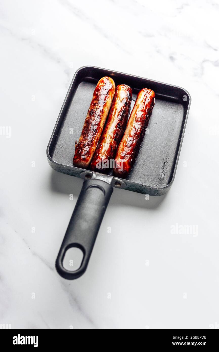 Salsicce di maiale cotte in una piccola padella senza bastone su uno sfondo di marmo – FOODPIX BIANCO Foto Stock
