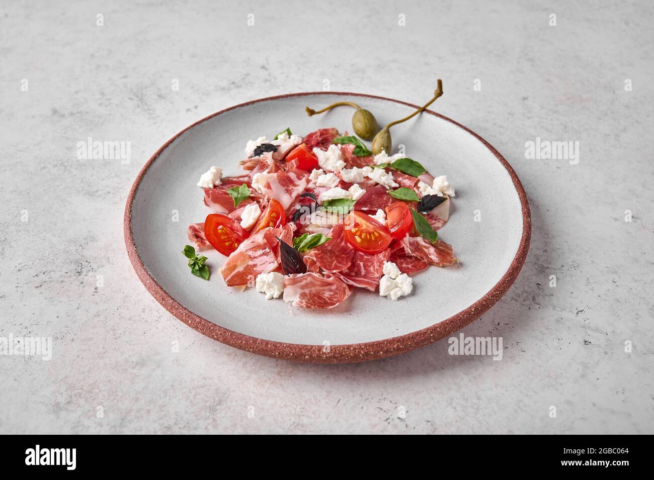 Prosciutto coppa di parma fette di ricotta, pomodoro, capperi e basilico su piatto leggero, primo piano Foto Stock