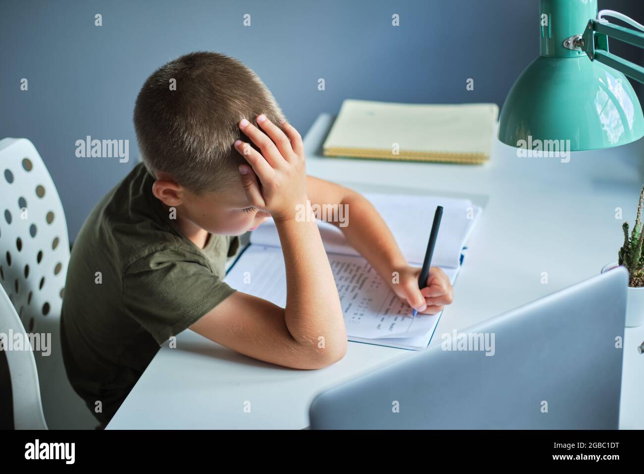 Lo scolaro seduto al tavolo e utilizzando il computer portatile mentre si lavora a casa. Concetto di homeschooling. Foto Stock