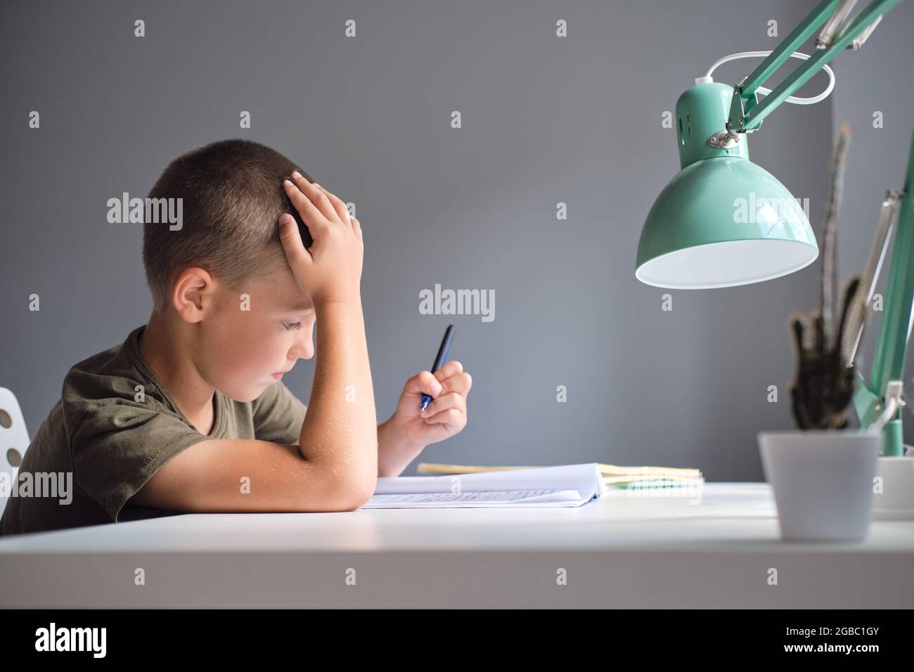Il ragazzo seduto al tavolo e facendo il lavoro scolastico a casa. Concetto di homeschooling. Foto Stock