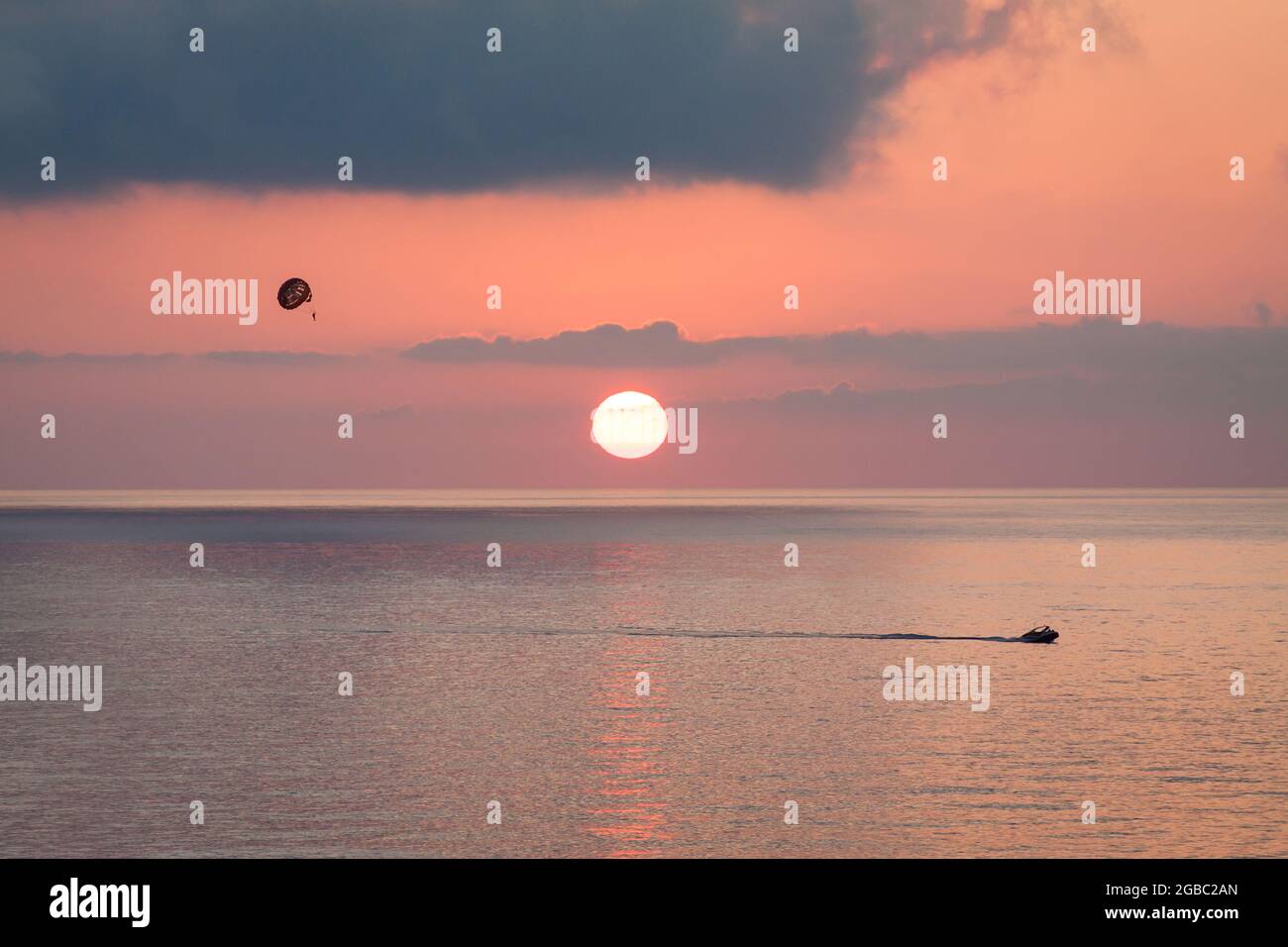 Parasailing dietro una barca al tramonto sul mare con il sole scende. Silhouette di una persona con paracadute contro il cielo di sera con le nuvole. Bella stagione. Foto Stock