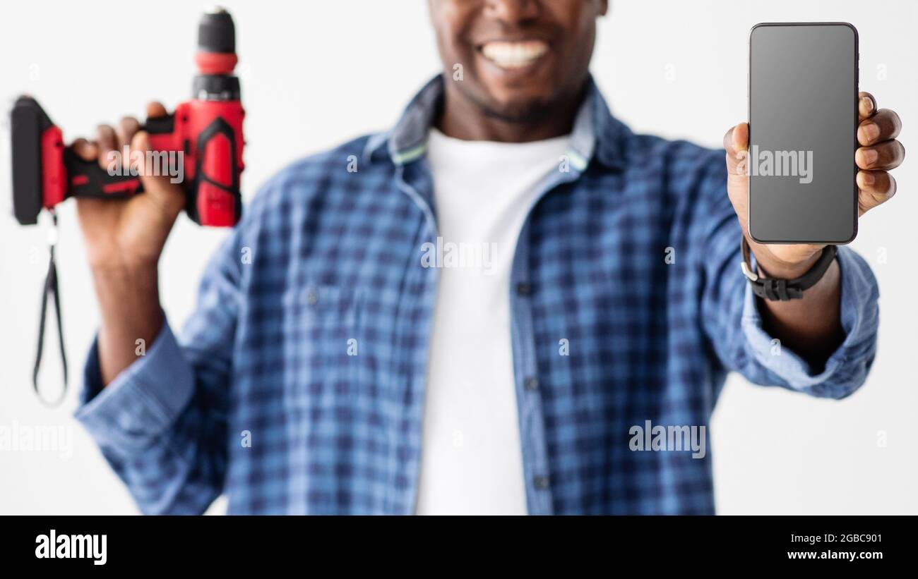 Handyman afro-americano che offre app, servizi o siti Web mobili, mostrando lo schermo vuoto dello smartphone alla fotocamera Foto Stock