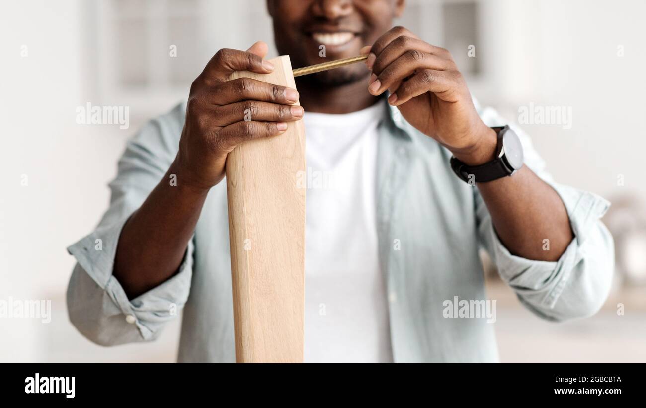 Felice uomo afro-americano avvitamento bullone a tavola di legno, installazione scrivania da soli a casa, primo piano, raccolto Foto Stock