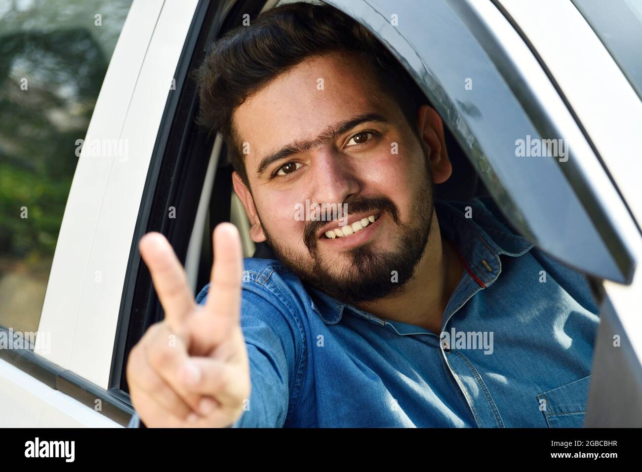 Felice uomo indiano mostrando segno di vittoria dalla vettura Foto Stock