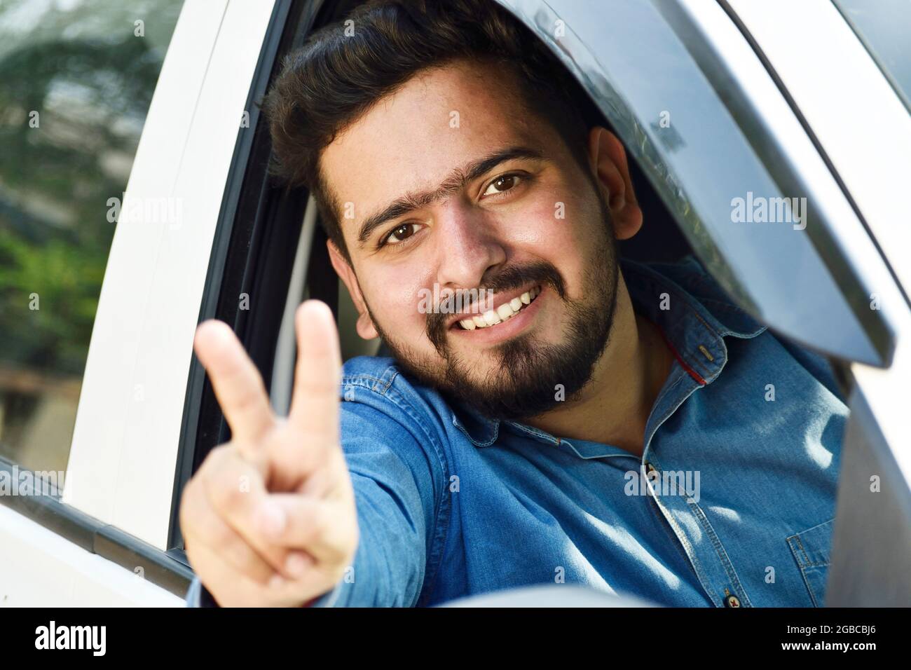 concetto di prestito auto, uomo indiano felice mostrando segno di vittoria dalla finestra dell'auto Foto Stock