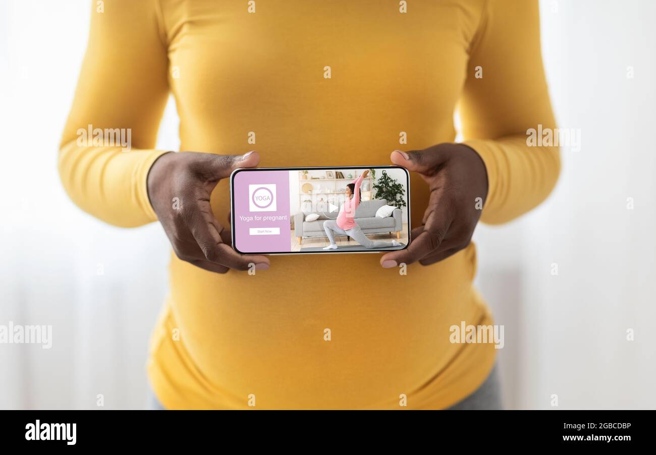 Giovane nero wonan utilizzando l'applicazione mobile per lo yoga durante la gravidanza Foto Stock