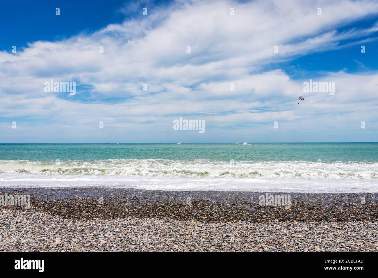 Bellissima spiaggia di ciottoli vuota a Batumi, Georgia. Barca con parapendio. Estate brillante giorno di sole, acqua blu. Nessuna gente. Foto Stock