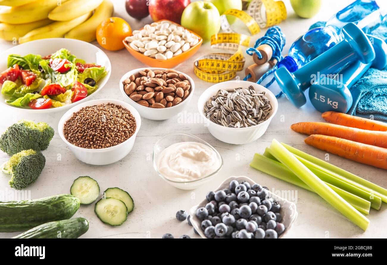 Selezione di alimenti sani, verdure, frutta, mandorle, insalata, attrezzi da esercizio e nastro di misurazione. Foto Stock