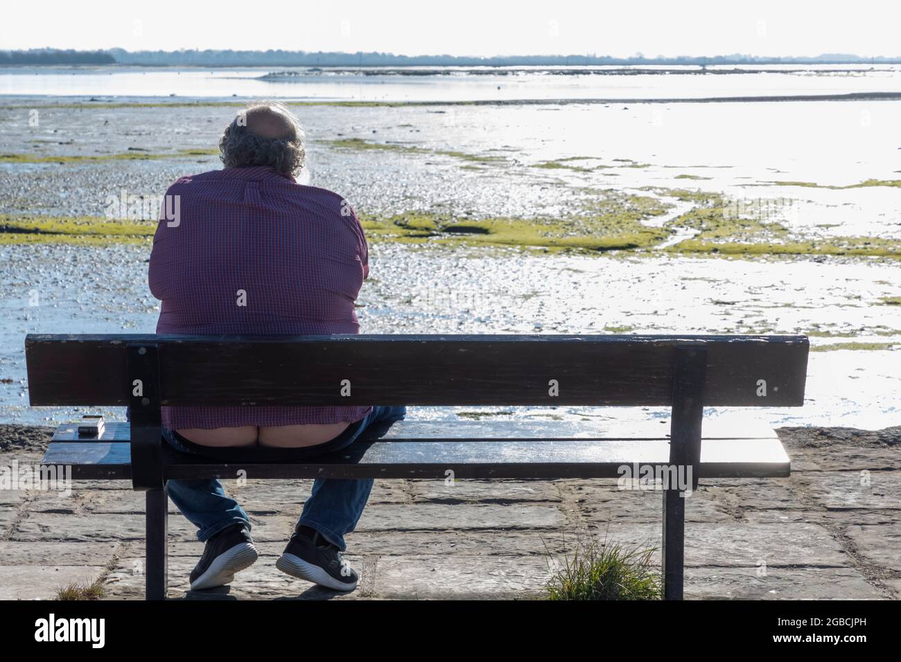 Inghilterra, Hampshire, Hayling Island, Funny vista posteriore immagine di uomo in sovrappeso seduto su Bench Foto Stock
