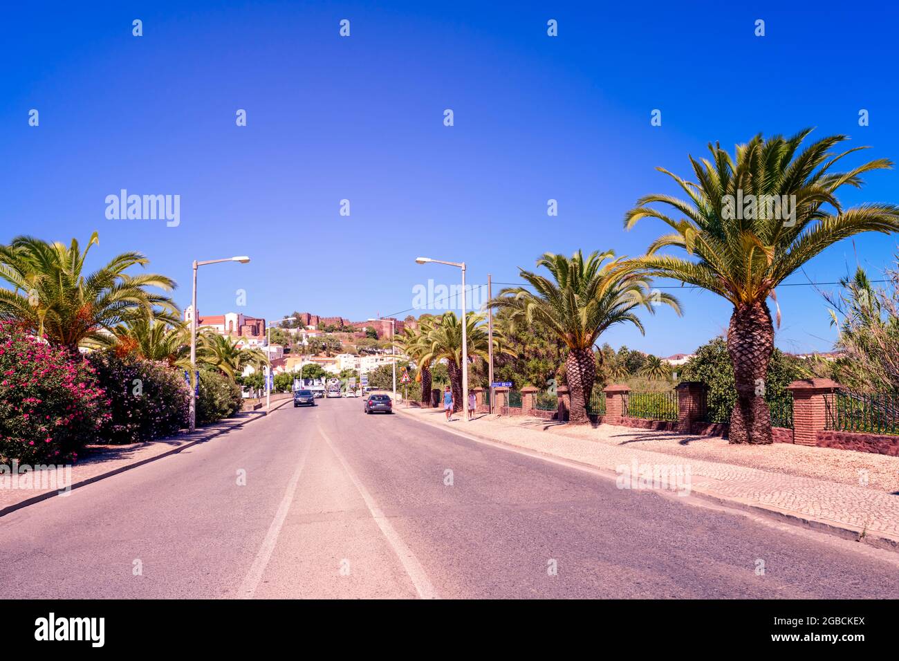 La strada principale in Silves fiancheggiata da palme attraverso una brige sul fiume Arade. Il castello di Silves può essere visto sullo skyline Foto Stock