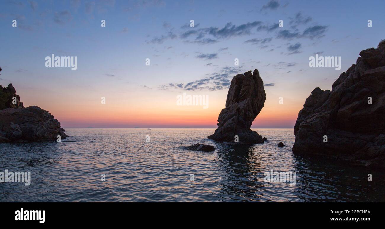 Cefalù, Palermo, Sicilia, Italia. Vista panoramica sulle acque tranquille della baia di Calura, all'alba, torreggianti formazioni rocciose che si stagliano contro il cielo colorato. Foto Stock