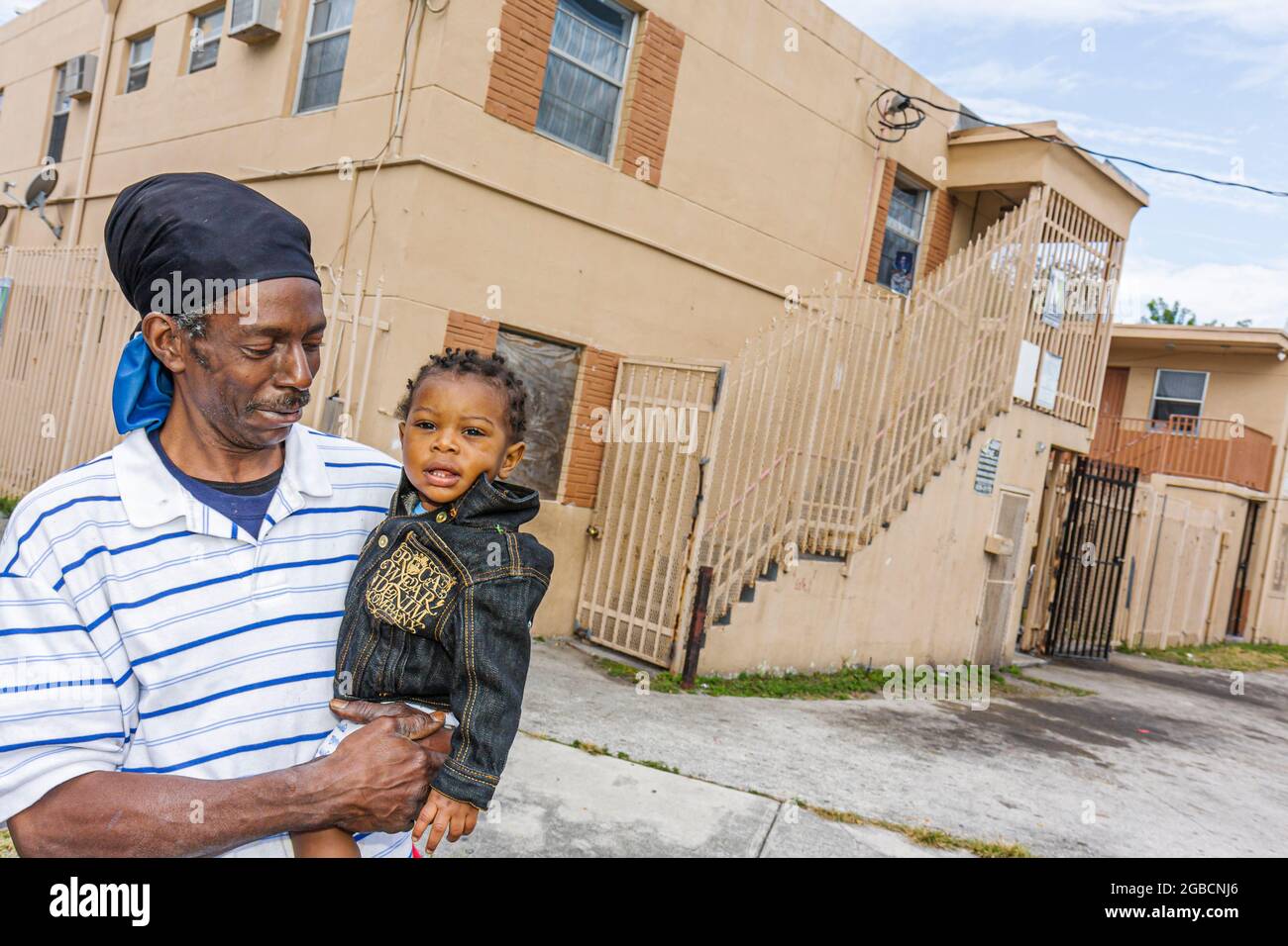 Miami Florida,Overtown,città interna urbana a basso reddito uomo nero,ragazzo bambino nonno figlio genitore che trasporta le holds holding, Foto Stock