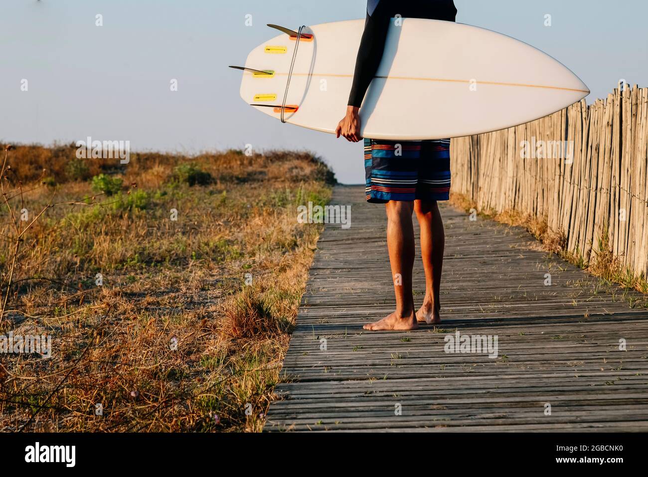 Giovane irriconoscibile surfer tiene una tavola da surf quando la spiaggia si innamora, sport estremo, sano ed esercitandosi. Foto Stock