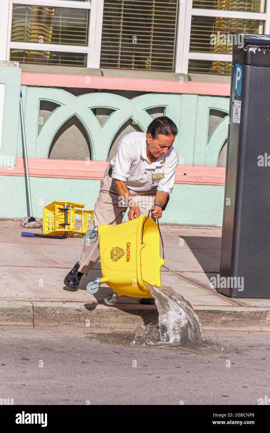 Miami Beach Florida, Ocean Drive, uomo ispanico janitor lavoratore dipendente personale pulizia, spazzolone scarico acqua sporca strada marciapiede inquinato po Foto Stock