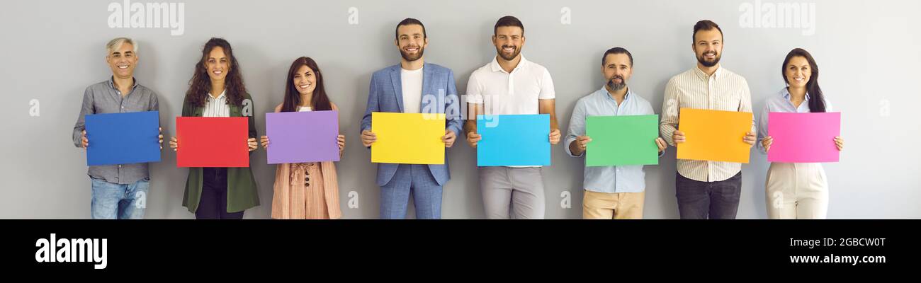 Intestazione con gruppo di persone felici in piedi accanto alla parete dello studio e che tengono striscioni di carta mockup Foto Stock