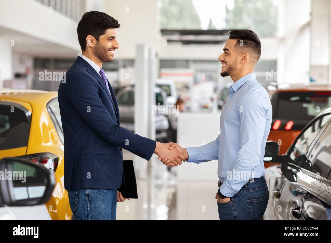Il responsabile di vendite saluta il ragazzo arabo bello, interno del salone dell'automobile Foto Stock