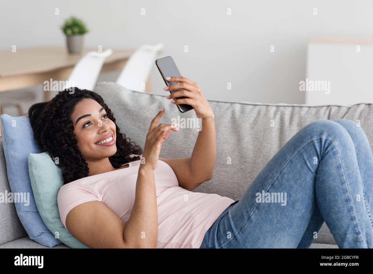Goditi il tempo libero da solo sul divano guardando le notizie al telefono, comodo, rilassante a casa, utilizzando la tecnologia Foto Stock