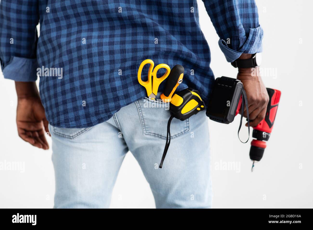 Utensile per foratura e fissaggio. Uomo afroamericano che tiene il trapano elettrico, il nastro di misurazione e le forbici in tasca Foto Stock