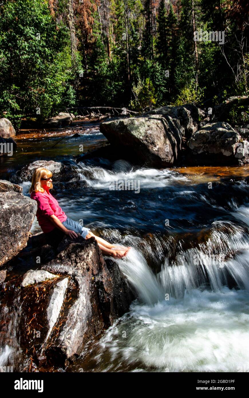 Giovane donna escursionista raffreddamento piedi in torrente di montagna, Rocky Mountain National Park, Colorado Foto Stock