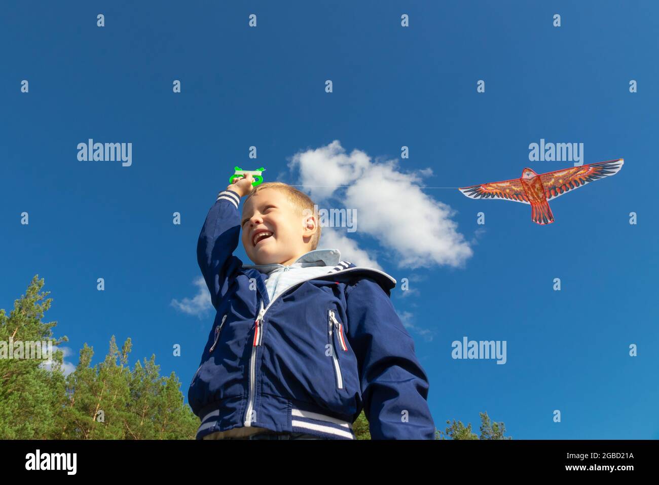 Un ragazzo di sei anni in giacca blu lancia un uccello aquilone in natura sullo sfondo di un cielo blu chiaro in una giornata estiva. Il luminoso Foto Stock