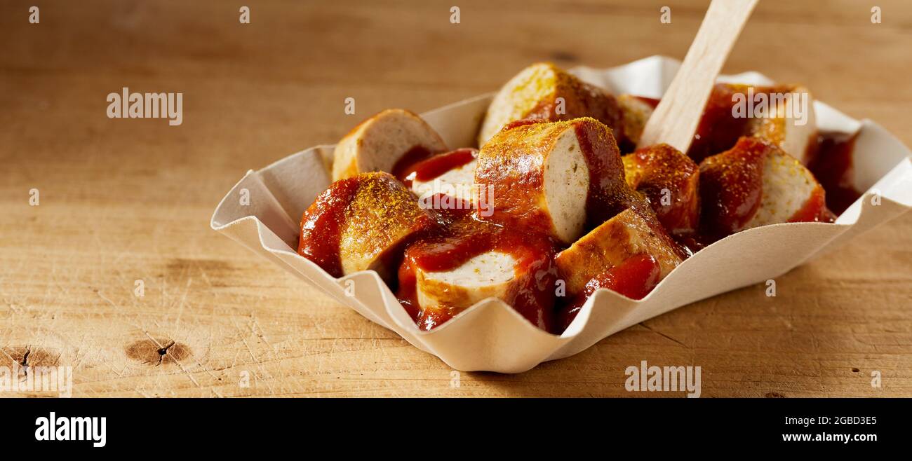 Delizioso piatto fast food di currywurst con ketchup e curry secco in ciotola per andare su sfondo marrone Foto Stock