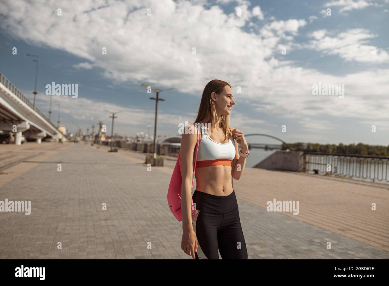 Donna in abbigliamento sportivo con zaino rosa si erge sul moderno argine cittadino Foto Stock