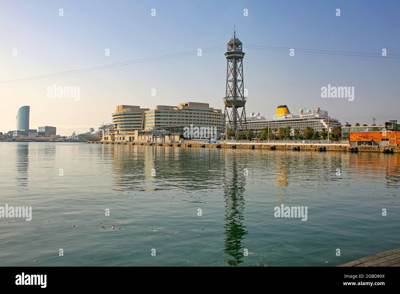 Vista attraverso il porto verso il terminal delle navi da crociera, con le navi ormeggiate, la torre della funivia, e riflessi nel Mar Mediterraneo, Barcellona, Spagna. Foto Stock