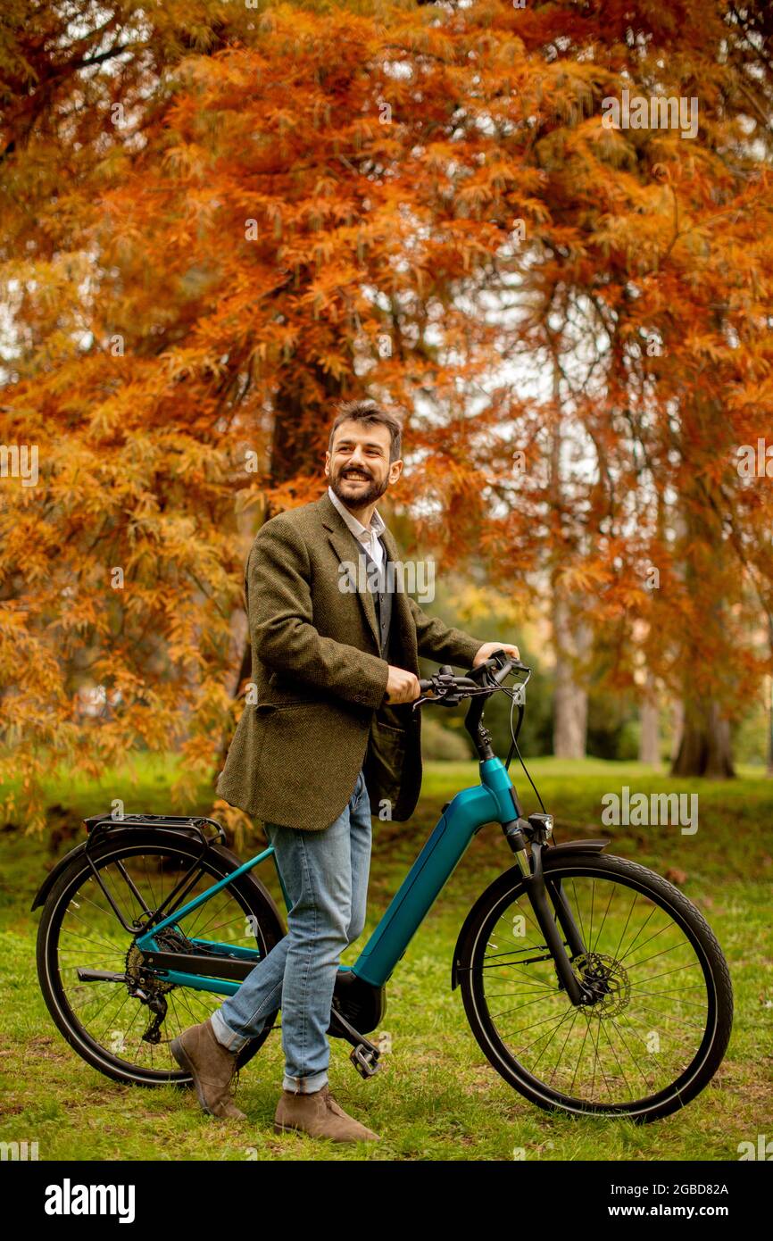 Bell'uomo giovane con bicicletta elettrica utilizzando il telefono cellulare in il parco autunnale Foto Stock