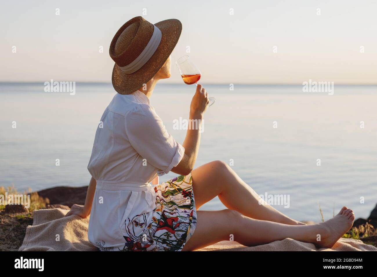 Bella signora in cappello di paglia con un bicchiere di vino sulla spiaggia. Foto Stock