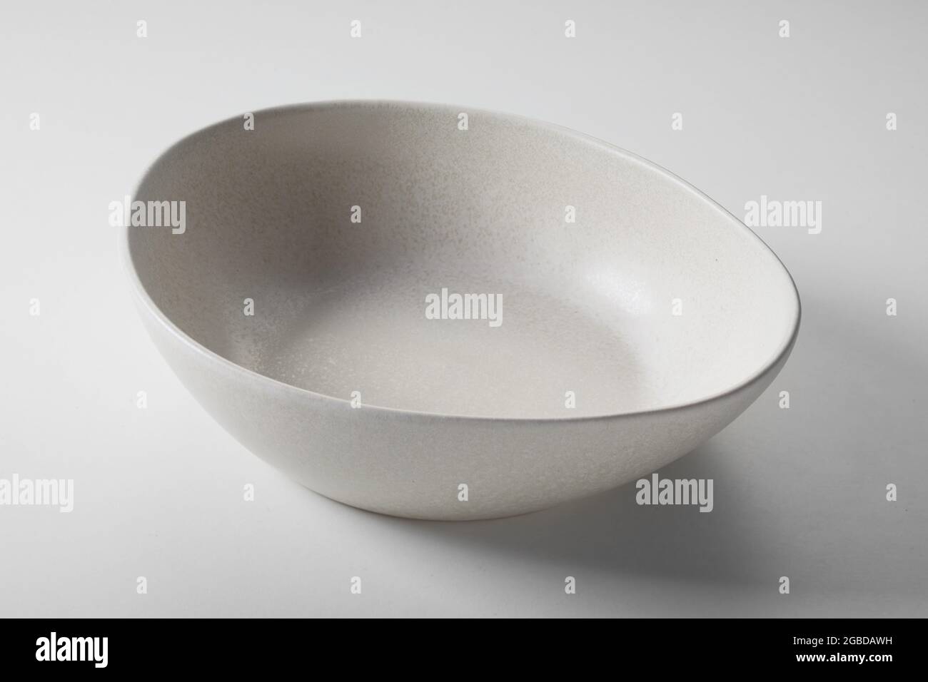 Alto angolo di ciotola vuota di ceramica di forma rotonda beige posta su un tavolo bianco Foto Stock