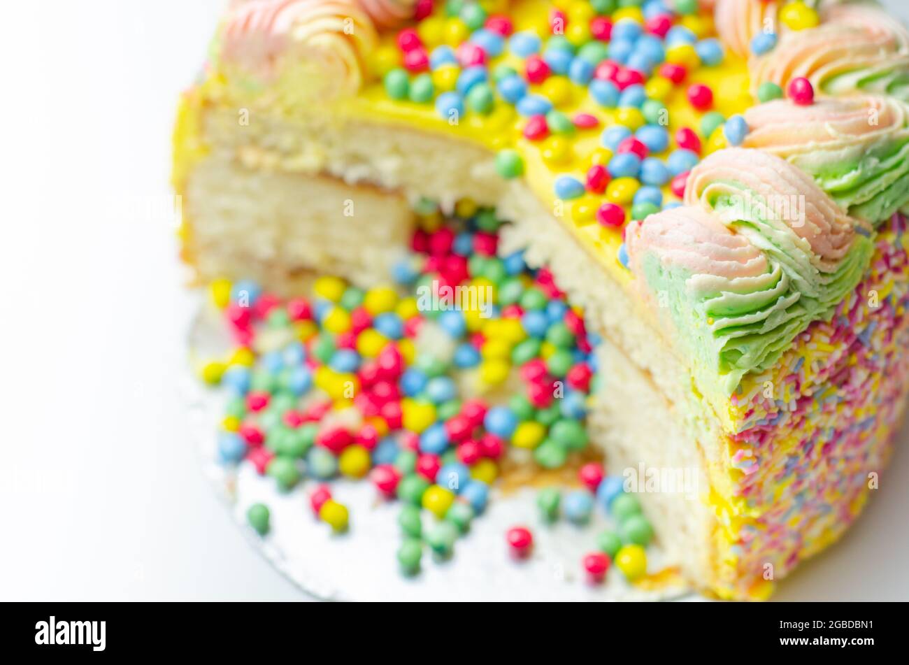 Spugna Madeira rivestita con glassa di colore giallo, stratificata con confettura di prugne e lamponi, ripiena e ricoperta di pennini di cioccolato multicolore e decorata Foto Stock