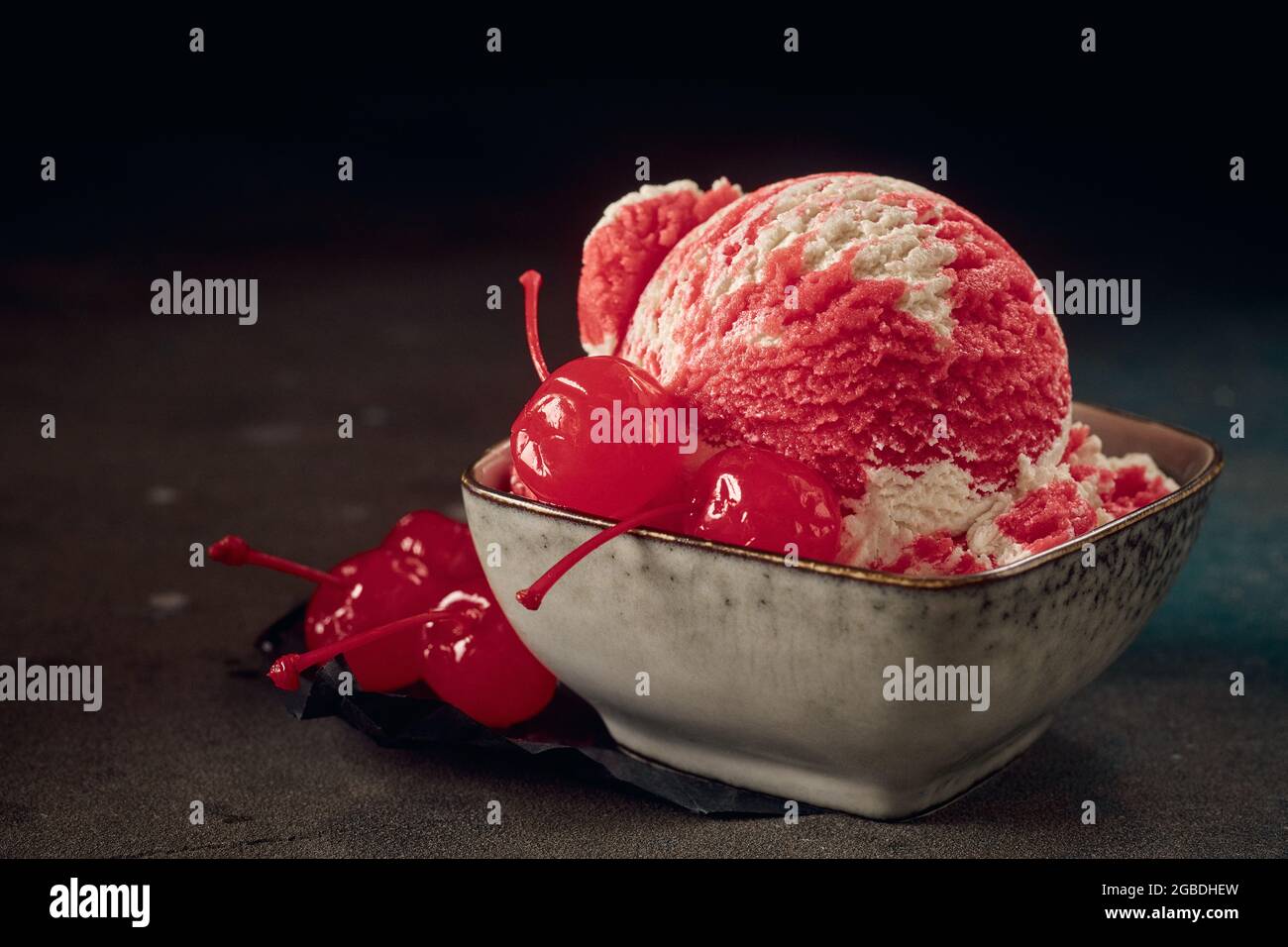Porzione di paletta per gelato rosso con ciliegie dolci di maraschino in ciotola su fondo scuro Foto Stock