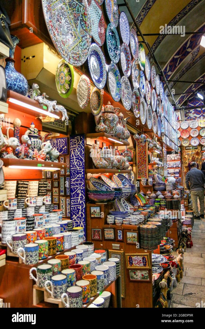 Vista ravvicinata degli scaffali esterni di un negozio di souvenir, con una varietà di ceramiche colorate in stile Iznik, tra cui piatti, piastrelle, vasi, tazze, e teapots, con un uomo, con un maglione a righe e pantaloni kaki, e rivolto lontano dalla telecamera sullo sfondo, pavimenti lastricati in pietra visibile all'estrema destra, E con un arco dipinto e piastrellato in blu, situato in un passaggio ad arco all'interno del Grand Bazaar, un grande quartiere dello shopping al coperto, costruito dagli Ottomani tra il XV e il XVIII secolo, nel quartiere Fatih di Istanbul, Turchia, il 11 novembre 2017. (Foto di Smith Coll Foto Stock