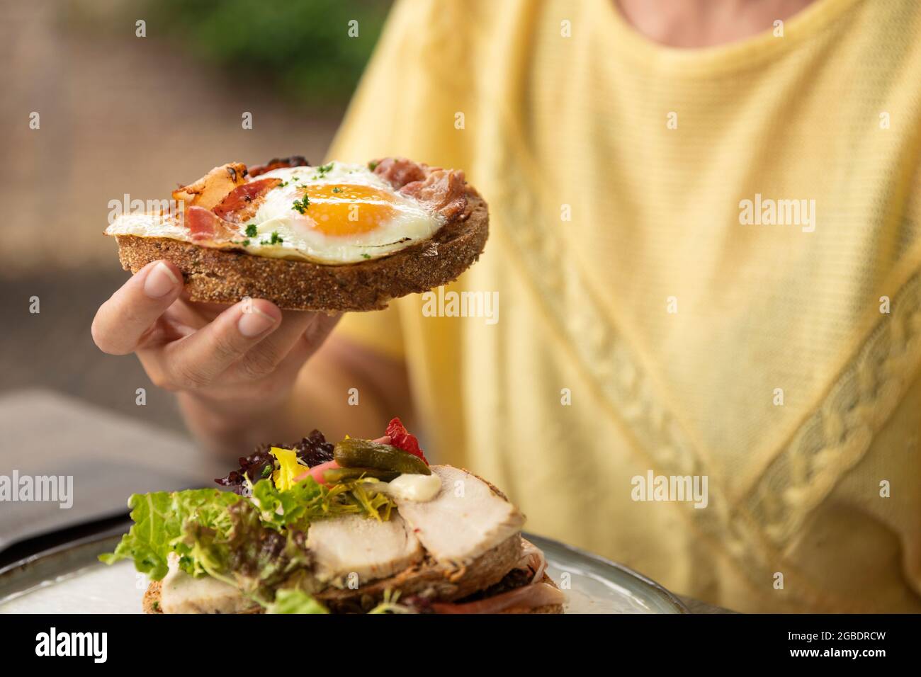 Donna che mangia un sano piatto sandwich fatto in casa club con ingredienti freschi come pomodoro, insalata, lattuga, pancetta, cavolfiore e pollo e un soleggiato s. Foto Stock